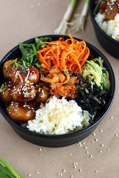 two black bowls filled with food on top of a brown table next to green onions and carrots