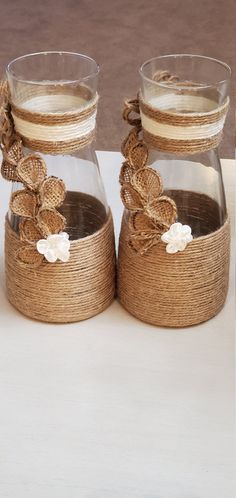 two glass vases sitting on top of each other with burlocks and flowers in them