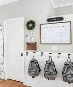 three backpacks hanging on hooks in front of a wall with a calendar and ruler