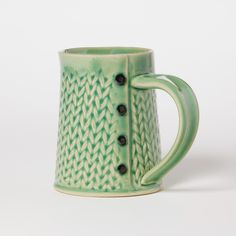 a green coffee mug with black buttons on the side and a design on the inside