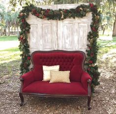 a red couch sitting in front of a white door covered in greenery and poinsettia