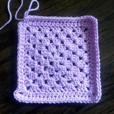 a purple crocheted square on a wooden table with a white string hanging from it