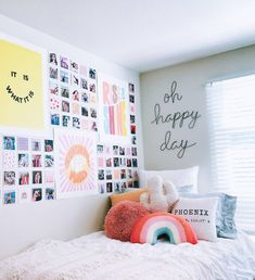 a bedroom with many pictures on the wall and a bed in front of it that has a rainbow pillow