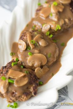 a piece of meat covered in mushroom gravy on a white plate with green onions