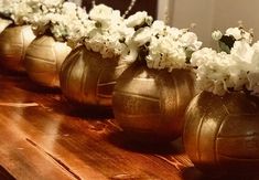 four gold vases filled with white flowers sitting on a wooden table in front of a mirror