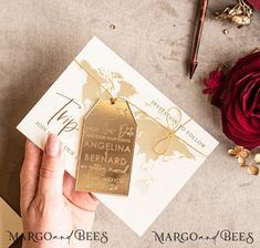 a person holding up a gold tag on top of a piece of paper next to a red rose