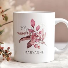 a white coffee mug sitting on top of a table next to a flower vase with pink flowers