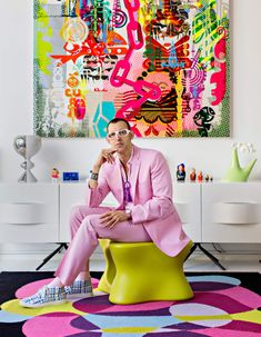 a man in a pink suit and tie sitting on a yellow chair next to a colorful painting