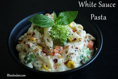 white sauce pasta with broccoli, carrots and other vegetables in a black bowl