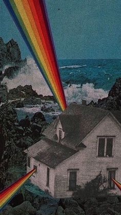 a house with a rainbow in front of it on the rocks near the ocean and waves