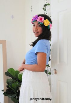 a woman wearing a flower crown standing in front of a door with her hands on her hips