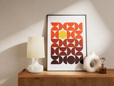 an orange and brown abstract art print on a wall next to a white vase with a lamp