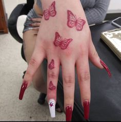 a woman's hand with red nail polish and butterfly tattoos on her left thumb