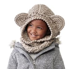 a young child wearing a crocheted hat and scarf with a bear ear flap