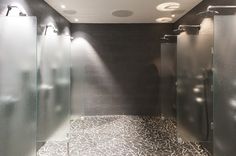 an empty bathroom with black and white tile on the floor, glass partitions in the shower