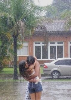 two people hugging each other in the rain with cars parked behind them and palm trees