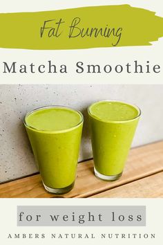 two glasses filled with green smoothie sitting on top of a wooden table next to a wall