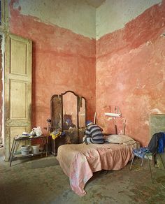 an old bedroom with pink walls and peeling paint on the walls, including a bed