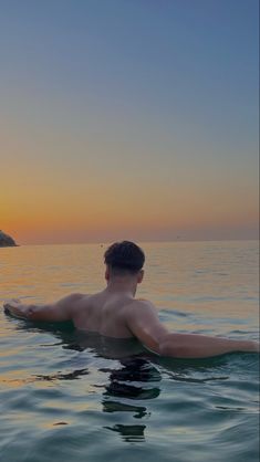 a man laying on top of a surfboard in the middle of the ocean at sunset