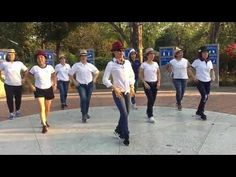 a group of people in white shirts and jeans are dancing on a sidewalk with trees behind them