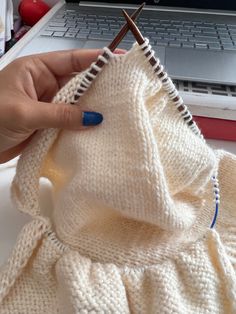 a woman is holding a knitted sweater in front of a laptop