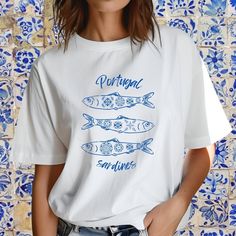 Celebrate the vibrant culture of Portugal with our exclusive oversized t-shirt featuring a charming sardines design! Perfect for those who love unique and stylish apparel, this t-shirt effortlessly combines comfort with a touch of Mediterranean flair. Add a touch of Portuguese charm to your wardrobe with our oversized sardines t-shirt. Order yours today and embrace the spirit of Portugal in style! PLEASE NOTE that your purchase is custom printed, unfortunately we do not allow returns or exchanges. All shirts are made with 100% airlume, ring-spun and combed cotton for extra softness. (Athletic Heather is 90% / 10% airlume combed and ring-spun cotton / polyester) .: 100% airlume combed and ring-spun cotton .: Medium fabric (6.0 oz/yd² (170 g/m .: Relaxed fit .:Tear-away label IF you have any Casual White Fish Print Top, Summer Fish Print Crew Neck Tops, Summer Crew Neck Top With Fish Print, Cotton Short Sleeve T-shirt With Fish Print, White Casual Shirt With Fish Print, White Cotton Shirt With Fish Print, Short Sleeve Graphic Tee With Fish Print, White Short Sleeve Shirt With Fish Print, Casual Crew Neck T-shirt With Fish Print