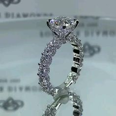 a close up view of a diamond ring on a glass surface with the reflection of it