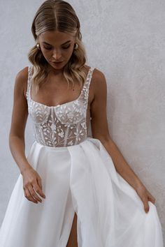 a woman in a white dress leaning against a wall