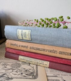 four books stacked on top of each other next to a flower pot with flowers in it