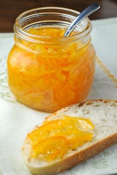 a jar of orange marmalade sits next to a slice of bread