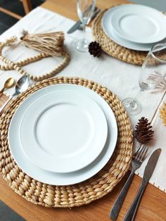 a place setting with pine cones on the table and white plates, silverware and napkins