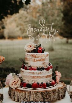 a wedding cake sitting on top of a tree stump with berries and flowers around it