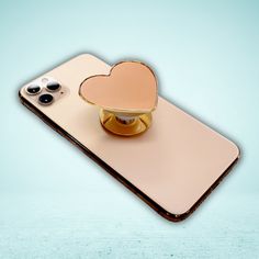 an iphone with a heart shaped holder attached to the back of it, sitting on top of a table