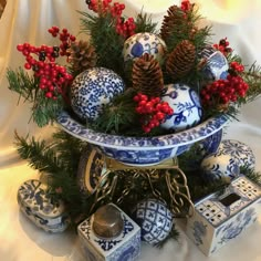 a blue and white christmas arrangement with pine cones, red berries, evergreen branches and other ornaments