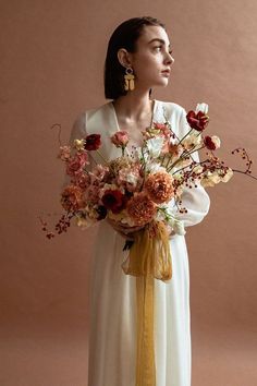 a woman wearing a white dress holding a bouquet of flowers in front of her face