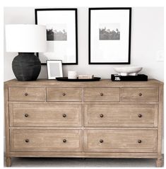 two framed pictures on the wall above a wooden dresser with drawers and lamps in front of it