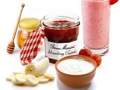 a jar of strawberry butter next to a bowl of sliced bananas and a cup of strawberries