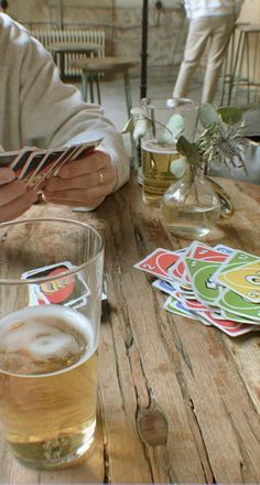 two people sitting at a table with beer and cards on the table next to them