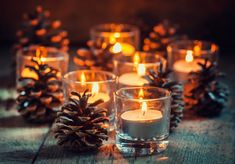 pine cones and candles are sitting on the wooden table, surrounded by small glass cups