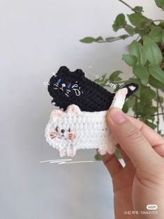 a hand holding a small crocheted cat and kitten brooch with another one in the background