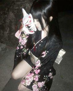 a woman with long black hair wearing a kimono and holding a white mask on her face