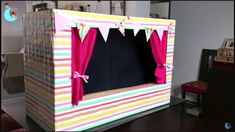 a play house made out of cardboard with red curtains and pink bows on the top