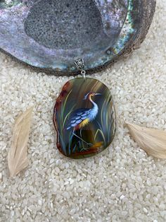 a bird is sitting on the ground next to some feathers and a glass pendant with an image of a crane