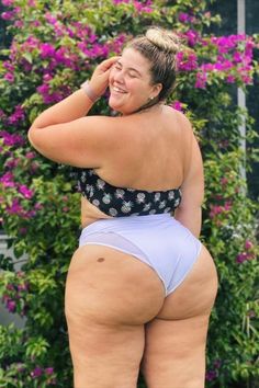 A woman smiling confidently while posing outdoors in a floral bikini top and white high-waisted bottoms. She stands in front of a lush garden with vibrant purple flowers. Plus Size Swimsuits, Outdoors Adventure, My Pictures, Lifestyle