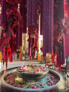 a fountain surrounded by pink flowers in a room with purple drapes hanging from the ceiling