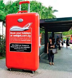 a red luggage bag sitting on the side of a road next to a bus stop