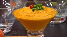 an orange dessert in a glass bowl on a table with other glasses and plates behind it