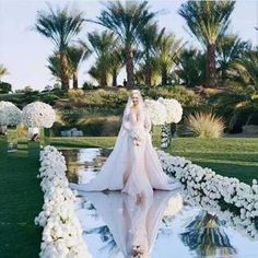 a woman in a wedding dress is walking down the aisle with flowers all around her