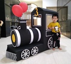 a young boy standing in front of a train made out of cardboards and balloons