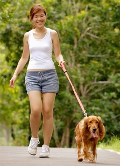 a young woman walking her dog on a leash in the park with trees behind her